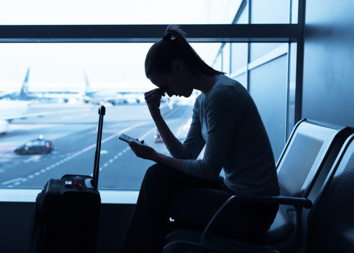 Silhouette of woman staring down at her phone, stressed, in an airport terminal