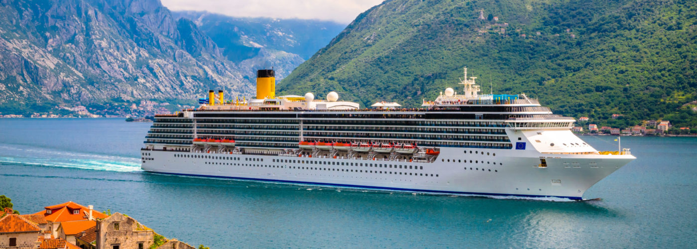 Cruise ship in water in front of lush green mountains