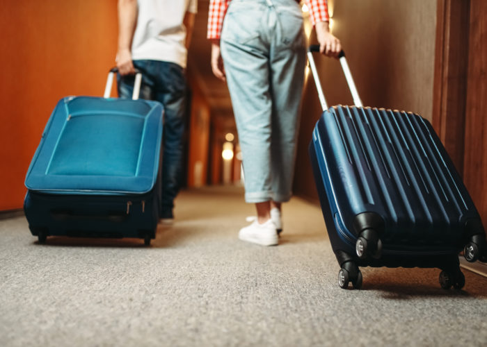 Two people wheeling rolling suitcases down a hotel hallway