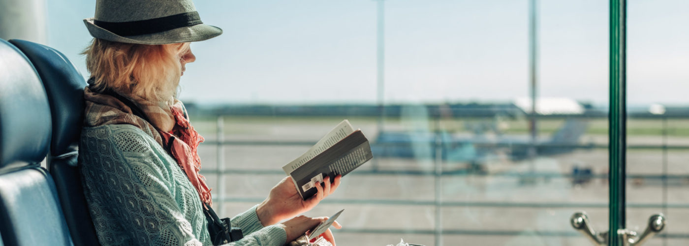 Woman reading book in front of a large window at an airport