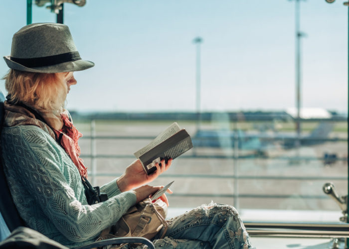 Woman reading book in front of a large window at an airport