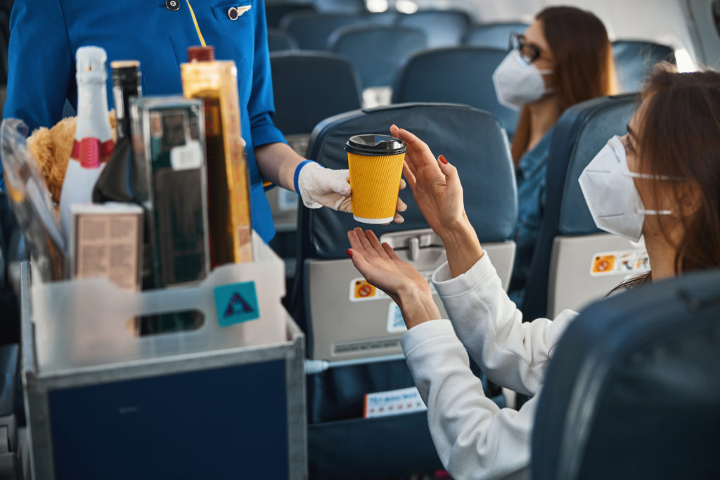 Woman wearing a face mask receiving a cup of coffee from a flight attendant on a plane